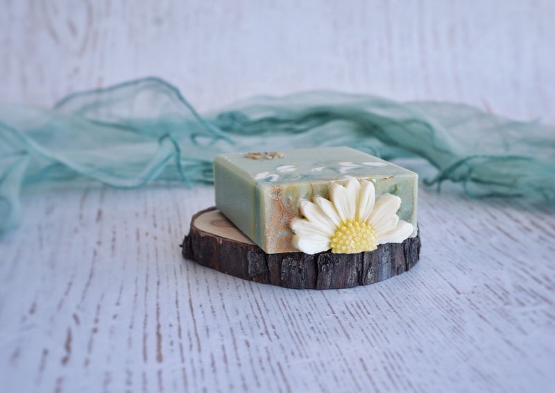 green base soap with white-green-yellow swirl decorated with half of a daisy flower styled on a piece of wood with leaves on the side
