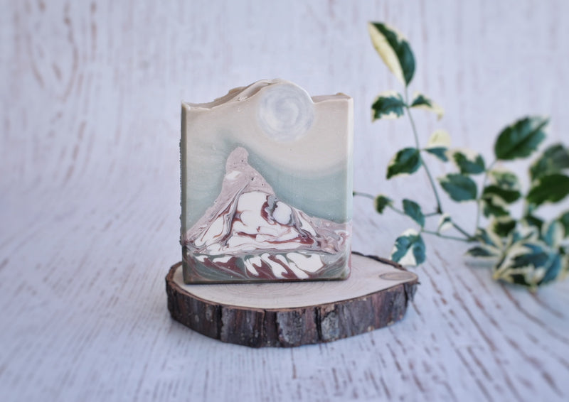 Landscape soap showing a mountain with a full moon embed as top decoration on a round wood surface 