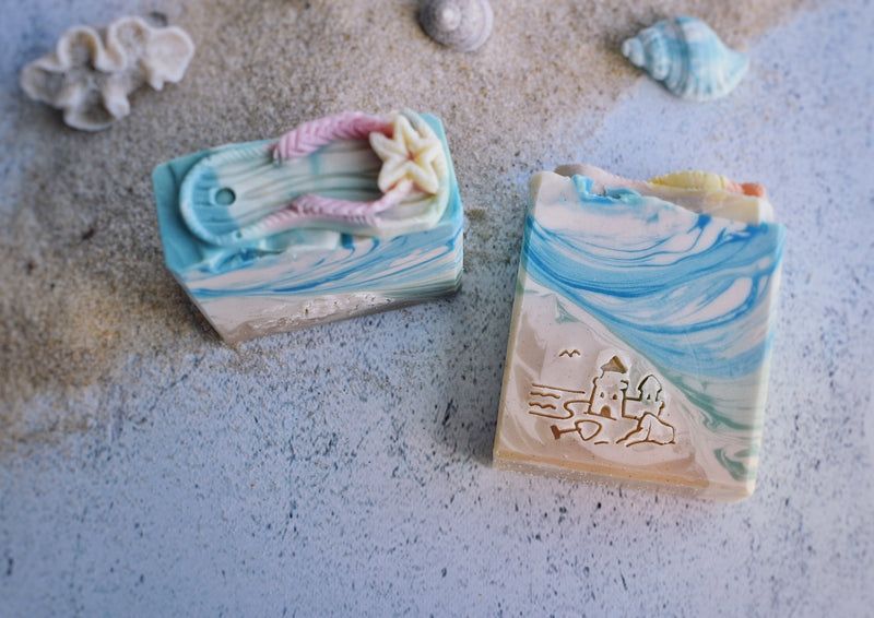 Sea themed soap with sand an blue part with a sand castle stamp on the soap and a soap thong on top of the soap as decoration 