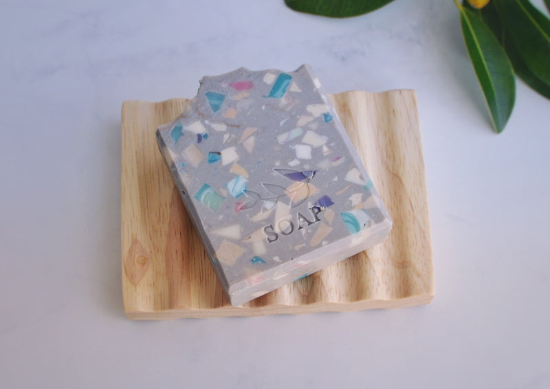 Grey soap with colourful soap pieces that look like confetti on a soap dish 