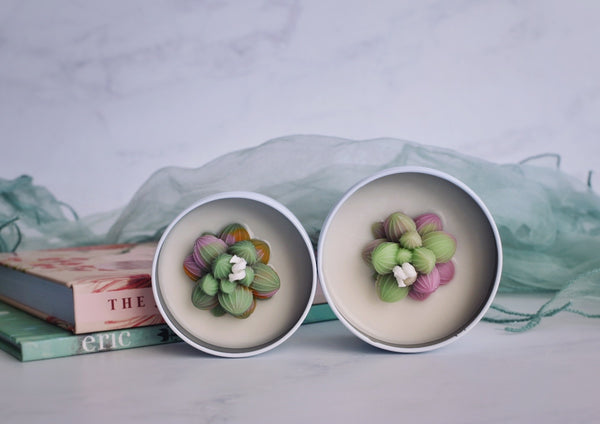 Two white tin candles with green pink succulent decoration on top 