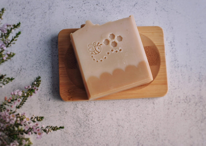 Beige soap with a bee stamping on a bamboo soap dish 