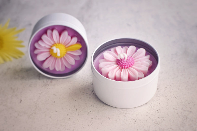 Two white tin candle pink wax base with pin petal daisy flower on top styled next to each other